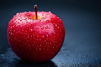 Fresh red apple with water drops on dark background, macro photography showing detailed texture and natural moisture on glossy fruit surface.