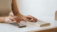 Professional woman typing on laptop keyboard while using smartphone for multitasking work productivity and digital communication at modern workspace.