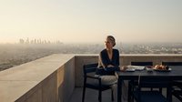 Professional woman enjoying sunset dinner on modern rooftop terrace overlooking city skyline. Urban lifestyle dining experience with panoramic views.