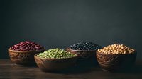 Red kidney beans, mung beans, black lentils and chickpeas in woven bowls on wooden surface. Legumes and pulses for cooking, nutrition and healthy eating.