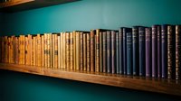Vintage books collection arranged on wooden shelf against turquoise wall creating cozy library atmosphere for reading and education concepts.