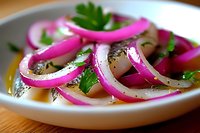 Fresh sliced red onions garnished with parsley and black pepper on white ceramic plate, close up view of vibrant pickled vegetable appetizer.