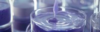 Liquid drop falling into purple viscous substance creating ripple effect in glass container, macro photography with selective focus and soft lighting.