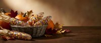 Autumn harvest corn cobs in wicker basket with colorful fall leaves on rustic wooden table creating warm seasonal thanksgiving decoration display.