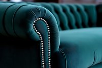 Close-up view of emerald green velvet Chesterfield sofa with silver nailhead trim detail showing luxurious tufted upholstery and curved armrest design.
