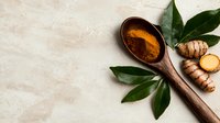 Fresh turmeric root and ground spice powder in wooden spoon with green leaves on light textured background, copy space for healthy cooking ingredients.
