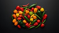 Colorful assortment of fresh hot chili peppers in red, orange, yellow and green varieties arranged on dark background for cooking and spice preparation.