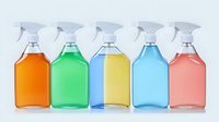 Colorful cleaning spray bottles in row on light background. Clear plastic containers filled with orange, green, blue, turquoise and pink liquid solutions.