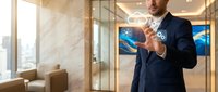Professional businessman in navy suit pointing forward in modern office lobby with marble walls and glass partitions during daytime.