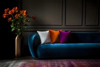 Modern dark interior with blue velvet sofa, colorful decorative pillows and orange flowers in copper vase against black wall. Moody luxury home decor setting.
