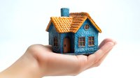 Miniature blue house with orange roof held in palm of hand against white background, symbolizing home ownership, real estate investment and property care.