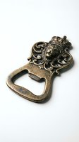 Antique brass bottle opener featuring ornate lion head with crown and decorative scrollwork, functional bar tool for home entertaining or collection display.