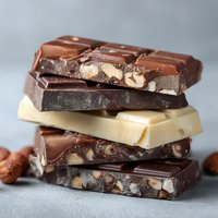 Stack of assorted chocolate bars with nuts on gray background, featuring milk, dark, and white varieties for dessert recipes and confectionery photography.