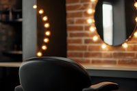 Modern salon interior with leather chair, exposed brick wall, round mirror and warm string lights creating cozy atmosphere for beauty services.