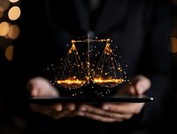 Glowing golden scales of justice hologram floating above smartphone, with hands holding device against dark background with bokeh lights effect.