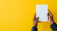 Hands of a man with dark skin tone holding blank white paper sheet against bright yellow background, suitable for advertising, marketing campaigns, and promotional materials.