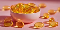 Golden omega-3 fish oil capsules in white ceramic bowl on pink background, nutritional supplement for health and wellness.