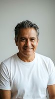 Smiling middle-aged Hispanic man with gray hair wearing white t-shirt against neutral background for lifestyle and wellness content.