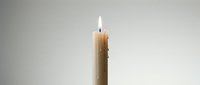 Single burning candle with bright flame against neutral background creating peaceful ambiance for meditation, relaxation, and spiritual moments.