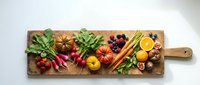 Fresh organic vegetables and fruits arranged on rustic wooden cutting board for healthy cooking and meal preparation in modern kitchen setting.