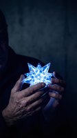 Elderly hands gently holding glowing blue crystal star with magical light rays in dark atmospheric setting for fantasy and spiritual concepts.