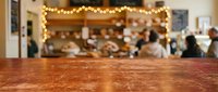 Wooden counter surface with blurred warm-lit cafe interior and string lights in background, suitable for product placement, hospitality marketing, and restaurant promotional materials.
