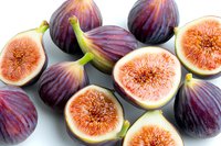 Fresh ripe purple figs whole and cut in half showing pink flesh and seeds on white background, organic healthy Mediterranean fruit composition.