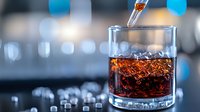 Droplet falling into glass of dark amber liquid with ice cubes creating splash effect, close-up shot against blurred bar background with bokeh lights.