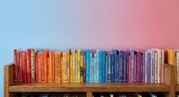 Colorful books arranged by rainbow spectrum on wooden shelf against gradient background for education and learning concepts.