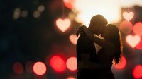 Romantic couple silhouette embracing against warm bokeh lights with heart shapes, love and intimacy concept for Valentine's Day celebrations.