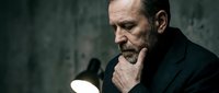 Thoughtful mature Caucasian businessman in dark suit contemplating under warm lamp light against textured wall background for corporate concepts.