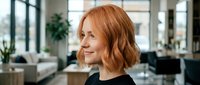 Professional redhead woman with bob haircut smiling in modern office workspace with natural lighting and contemporary furniture for business concepts.