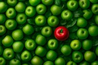 Single red apple stands out among many green apples, symbolizing uniqueness, leadership and individuality concept. Fresh fruit background with leaves.