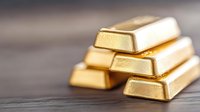Shiny gold bars stacked on dark wooden surface with selective focus and shallow depth of field, representing wealth, investment and financial security.