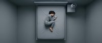 Young Asian man sleeping peacefully on bed using smartphone in modern minimalist bedroom with gray bedding and contemporary lighting fixtures.
