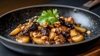 Homemade braised chicken with potatoes, prunes and walnuts garnished with fresh cilantro in black pan, close up view. Traditional comfort food recipe.