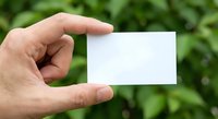 Hand holding blank white business card against green foliage background for mockup and branding presentation purposes.