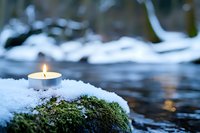 Peaceful winter scene with glowing candle on snow-covered moss by flowing stream. Serene nature meditation and mindfulness concept for wellness content.
