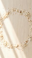 Scattered oat flakes and cereal crumbs arranged in a circular frame on light wooden surface with natural sunlight casting shadows.