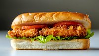 Crispy chicken sandwich with fresh lettuce and tomato on soft brioche bun, close-up view showing juicy breaded fillet and layered ingredients.
