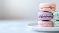 Pastel colored French macarons arranged on white plate against light background, soft focus composition showcasing delicate meringue-based confections.