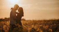 Romantic couple silhouette embracing in golden sunset field, intimate moment during golden hour creating warm atmospheric love scene for wedding concepts.