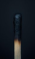 Burnt wooden matchstick with charred black head against dark background showing fire damage and combustion aftermath for safety concepts.