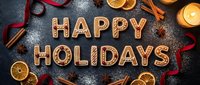 Happy Holidays gingerbread cookie letters with cinnamon sticks, star anise, dried oranges, red ribbon, and candle on dark background with powdered sugar.