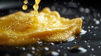 Melted cheese slice on dark surface with water droplets and steam, dramatic lighting captures golden texture and dripping motion in macro photography.