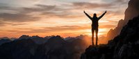 Male hiker celebrating success on mountain peak at golden sunrise with arms raised, dramatic landscape and warm sky colors creating inspirational moment.