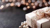 Elegant white gift box with shimmering rose gold ribbon and scattered pearls against dark background with festive bokeh lights. Luxury holiday celebration concept.