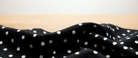 Crumpled black fabric with white polka dots against warm beige background, suitable for textile, fashion, and design projects.