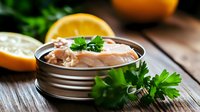 Fresh tuna salad with parsley garnish in metal tin, served with orange slices on rustic wooden background, healthy protein meal preparation.