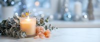 Glowing candle with eucalyptus branches and pink salt crystals on white surface. Soft bokeh lights create peaceful spa atmosphere for relaxation and wellness.